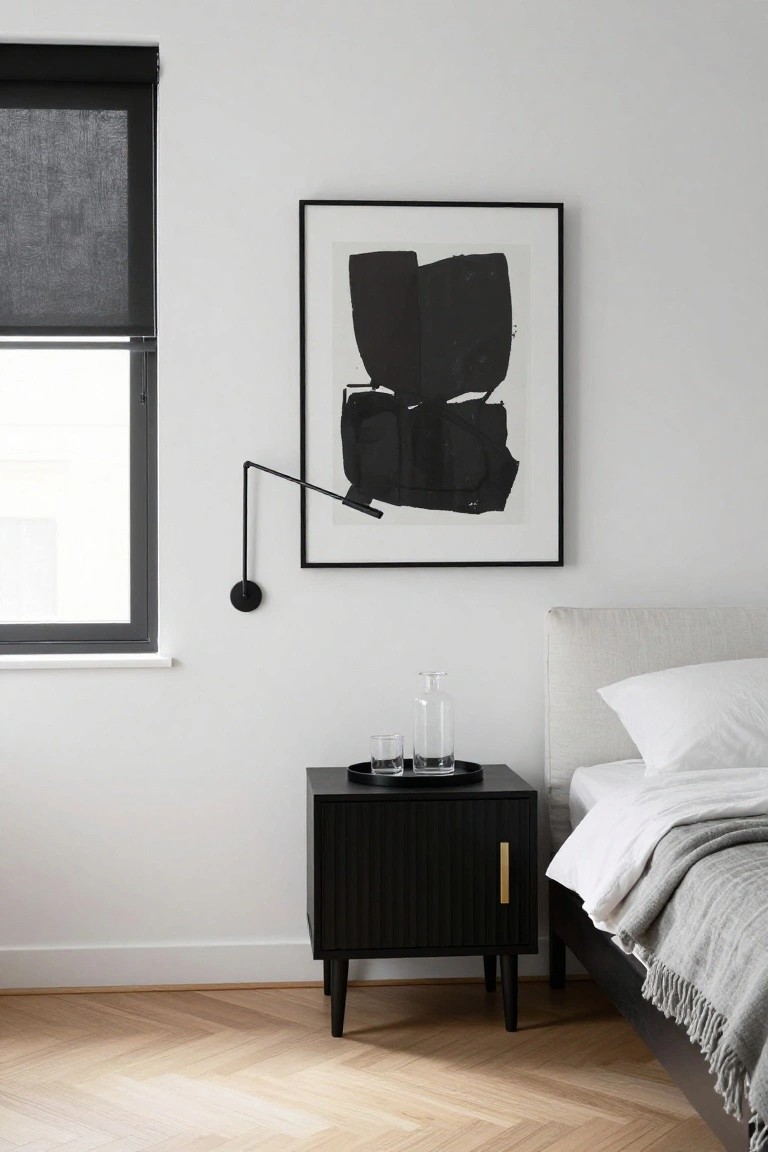 A minimalist bedroom with a black fluted nightstand beside a bed with white bedding and an abstract black and white artwork on the wall above it.