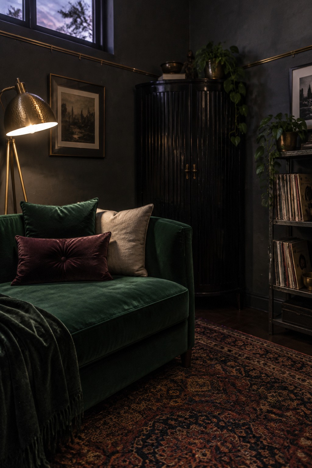 Green velvet sofa with burgundy pillows beside glowing brass lamp on patterned rug