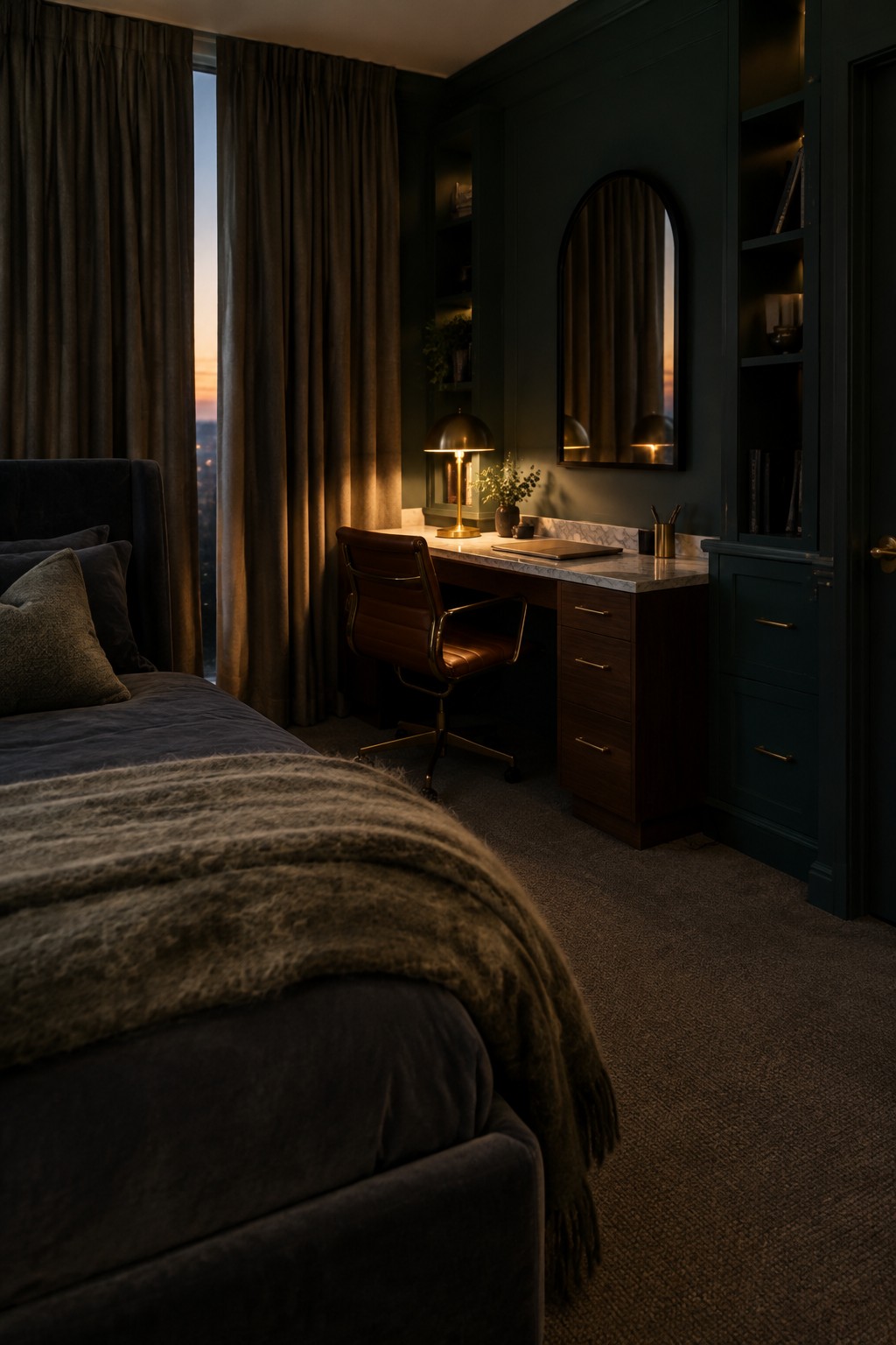 A bedroom interior with dark green built-in cabinetry, a wooden desk with drawers, a brown leather office chair, and an arched mirror above the desk.
