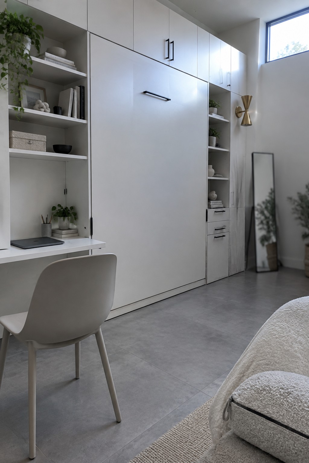 A minimalist interior with white floor-to-ceiling built-in cabinets, open shelving on both sides, an integrated white desk, a gray molded chair, and gray tile flooring.