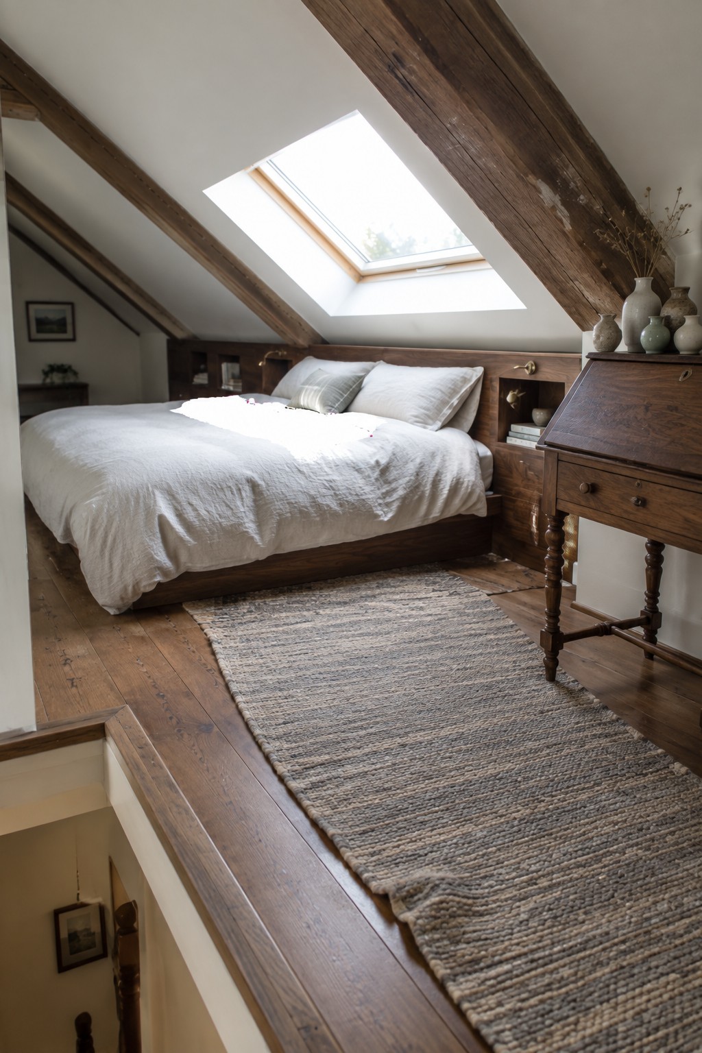 Cozy attic bedroom with wooden beams, skylight, white bedding, and woven rug