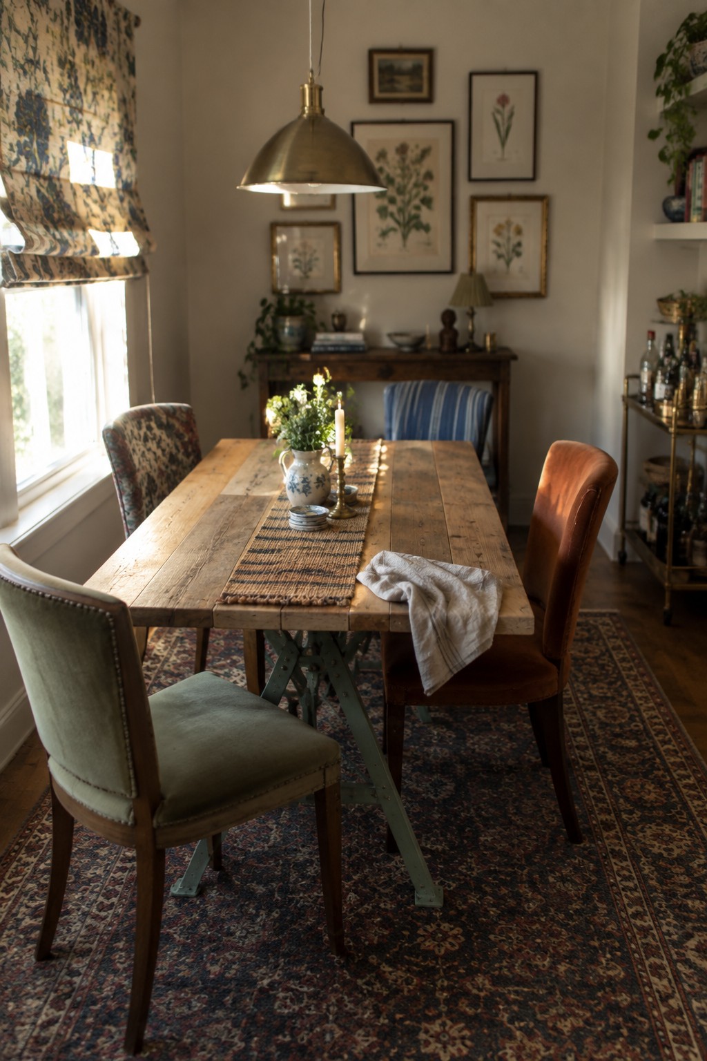 Rustic wooden dining table with mixed chairs under brass pendant light and botanical prints