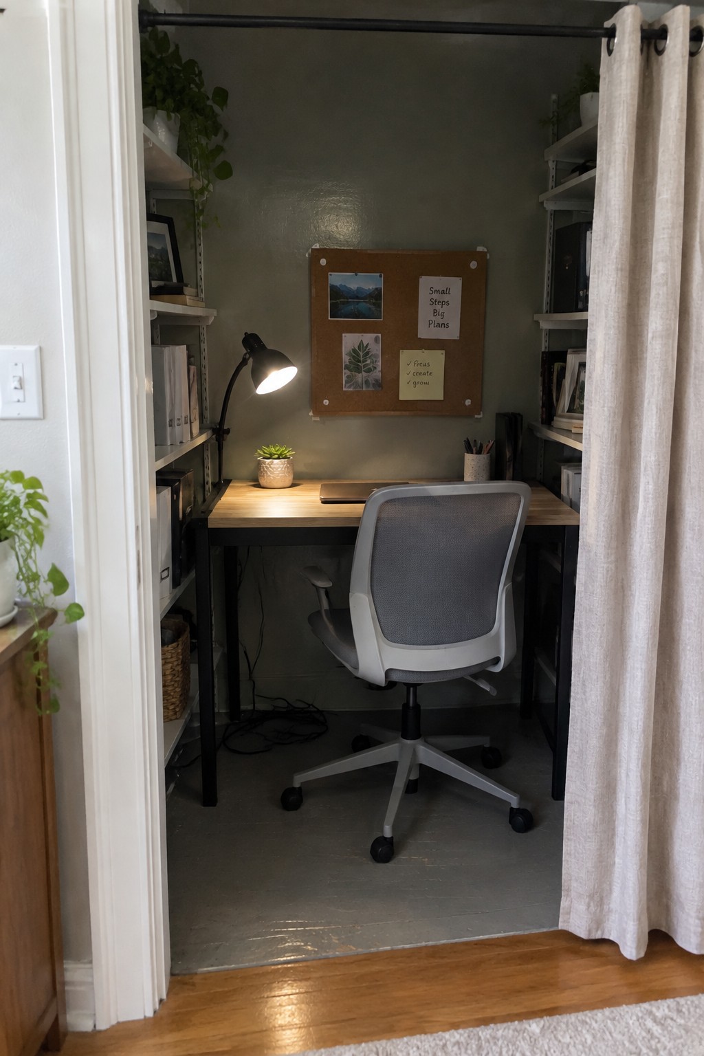 Small wooden desk and gray chair in closet office nook with lit lamp and corkboard.
