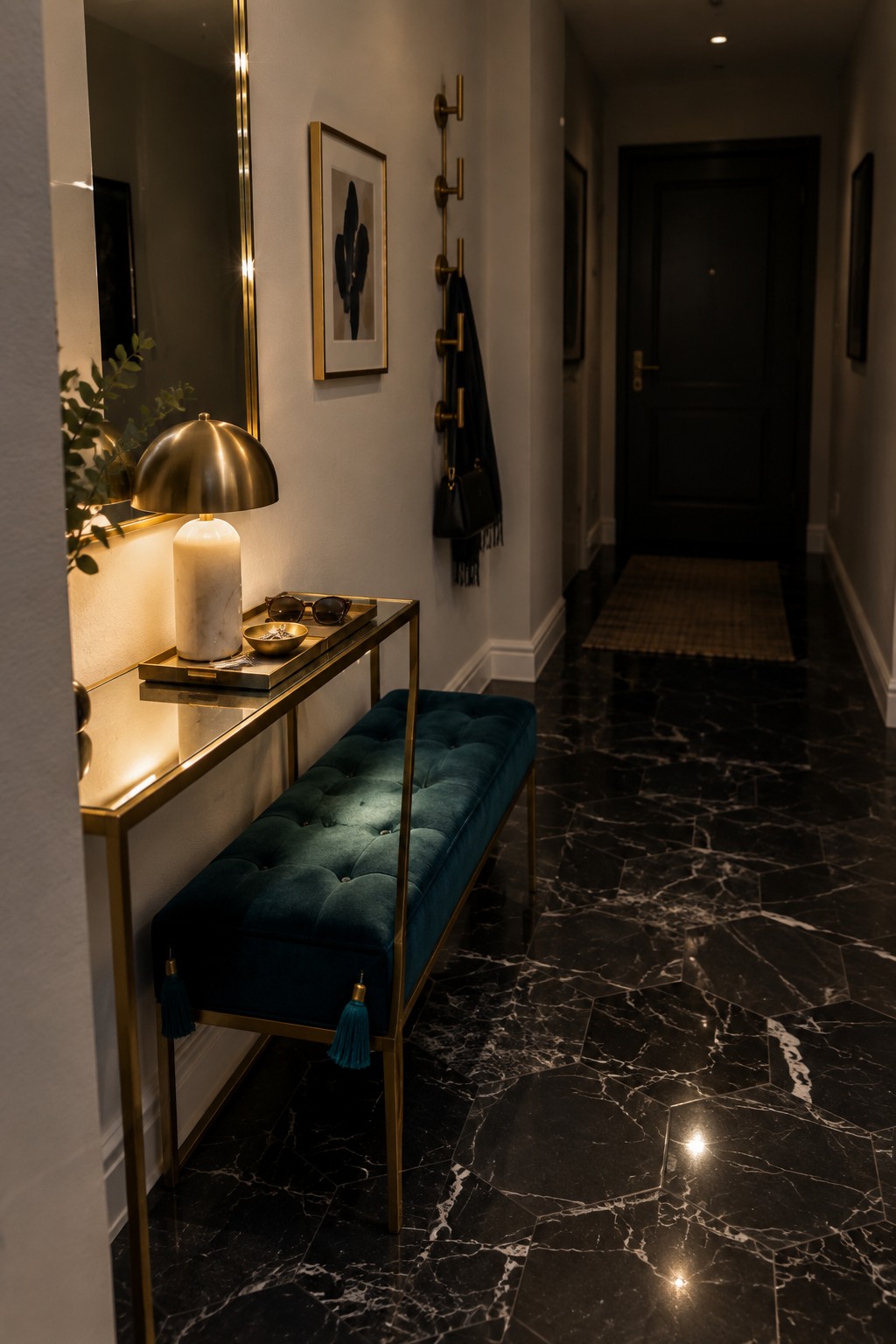A narrow entry hallway with a marble-topped console table, brass frame, white marble lamp, and teal tufted bench positioned underneath against a light wall with a mirror and black door at the end.